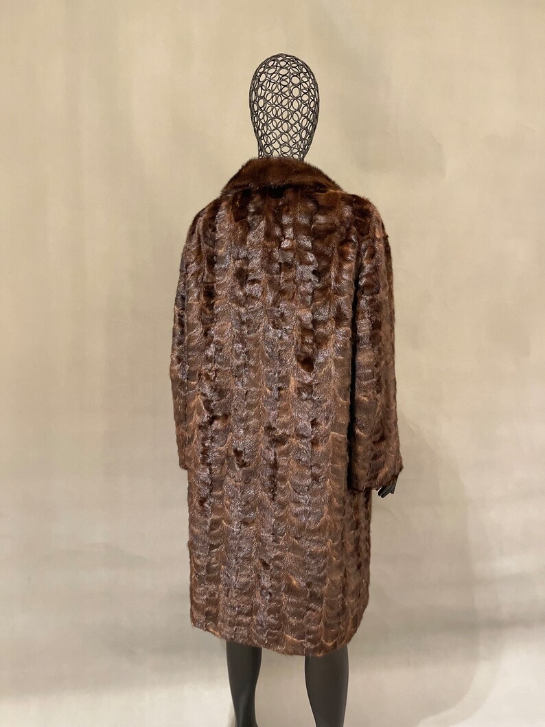 May include: A long brown fur coat with a collar. The coat is on a mannequin.