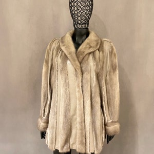 May include: A light grey fur coat with a collar and cuffs. The coat is lined with a smooth, light grey fabric.