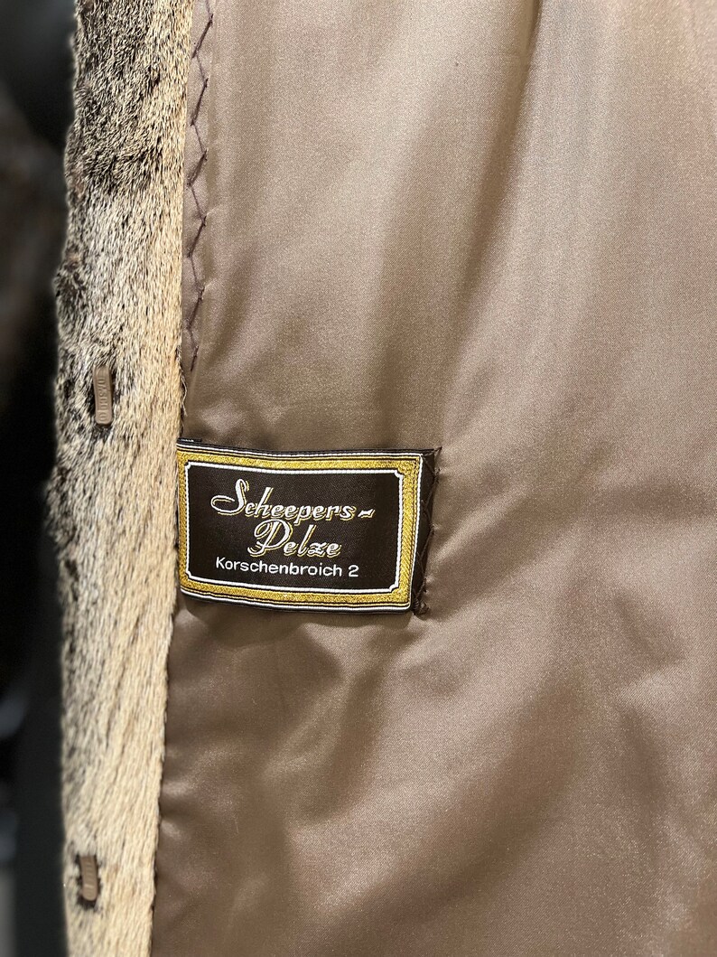 May include: A brown leather label with gold stitching and the text "Scheepers Pelze Korschenbroich 2" in a cursive font.