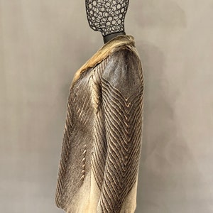 May include: A brown and white fur coat with a chevron pattern. The coat has a collar and is shown on a mannequin.
