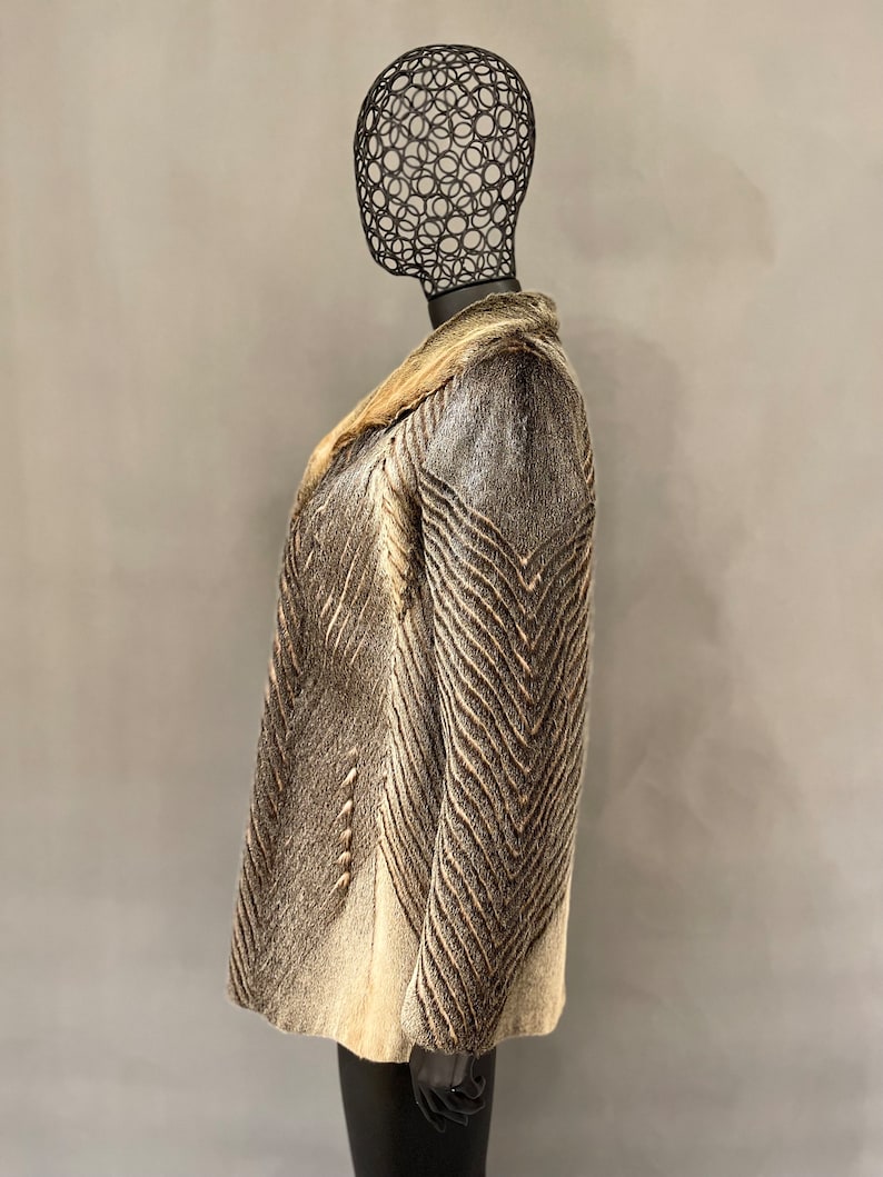 May include: A brown and white fur coat with a chevron pattern. The coat has a collar and is shown on a mannequin.