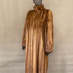 May include: A long brown fur coat with a high collar and a zipper closure. The coat is made of a soft, luxurious fur and has a sleek, elegant design.