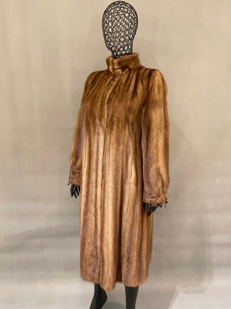 May include: A long brown fur coat with a high collar and a zipper closure. The coat is made of a soft, luxurious fur and has a sleek, elegant design.