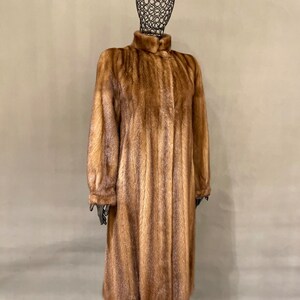 May include: A long brown fur coat with a high collar and a button closure.