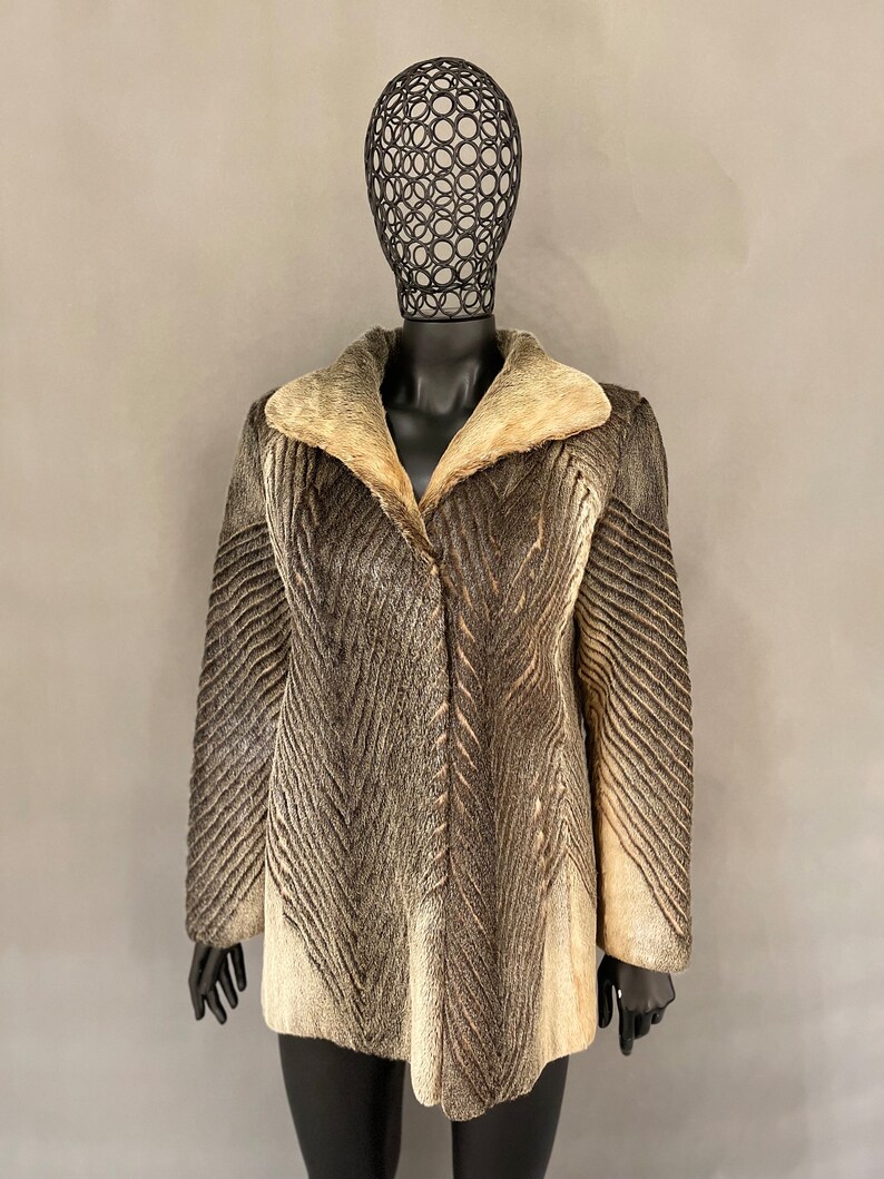May include: A brown and white fur coat with a large collar. The coat has a chevron pattern and is on a mannequin.