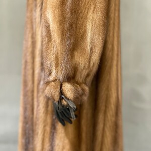 May include: A long brown fur coat with a striped pattern. The coat has a long sleeve with a tie at the cuff.