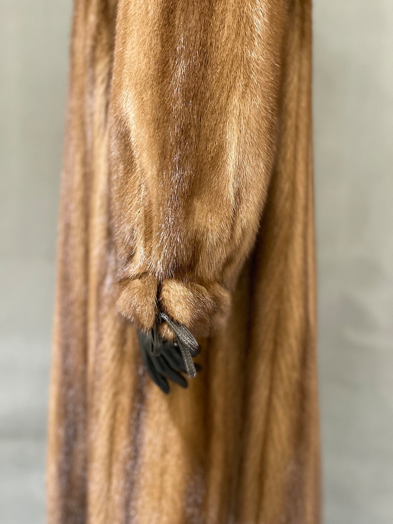 May include: A long brown fur coat with a striped pattern. The coat has a long sleeve with a tie at the cuff.