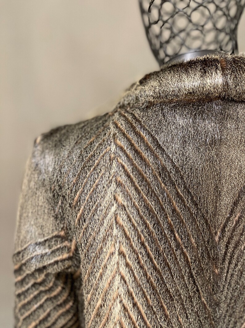 May include: A brown and white fur jacket with a chevron pattern. The jacket is made of a soft, luxurious fur.