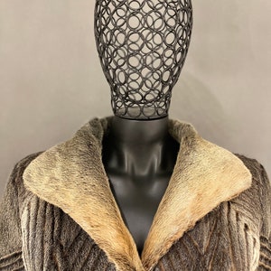 May include: A brown and gray fur coat with a large collar made of a lighter colored fur. The coat is on a black mannequin with a wire head.