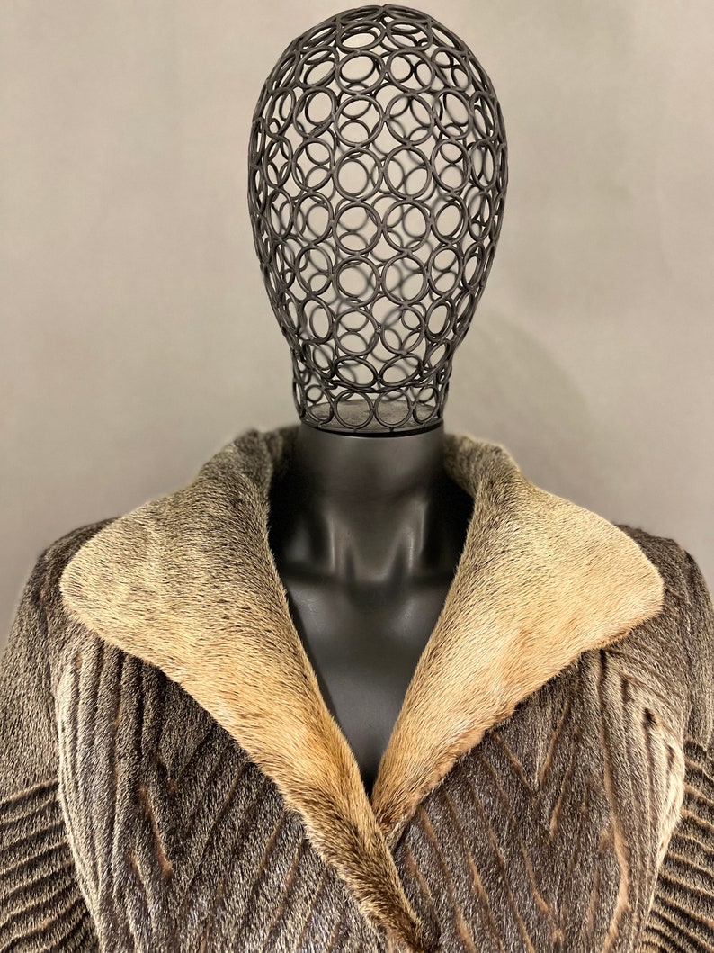 May include: A brown and gray fur coat with a large collar made of a lighter colored fur. The coat is on a black mannequin with a wire head.