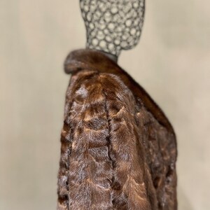 May include: A brown fur coat with a collar. The coat is on a mannequin.