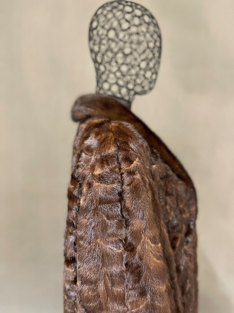 May include: A brown fur coat with a collar. The coat is on a mannequin.