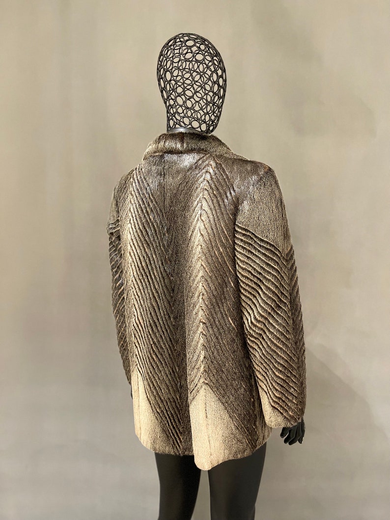May include: A brown and white fur coat with a chevron pattern. The coat is on a mannequin.