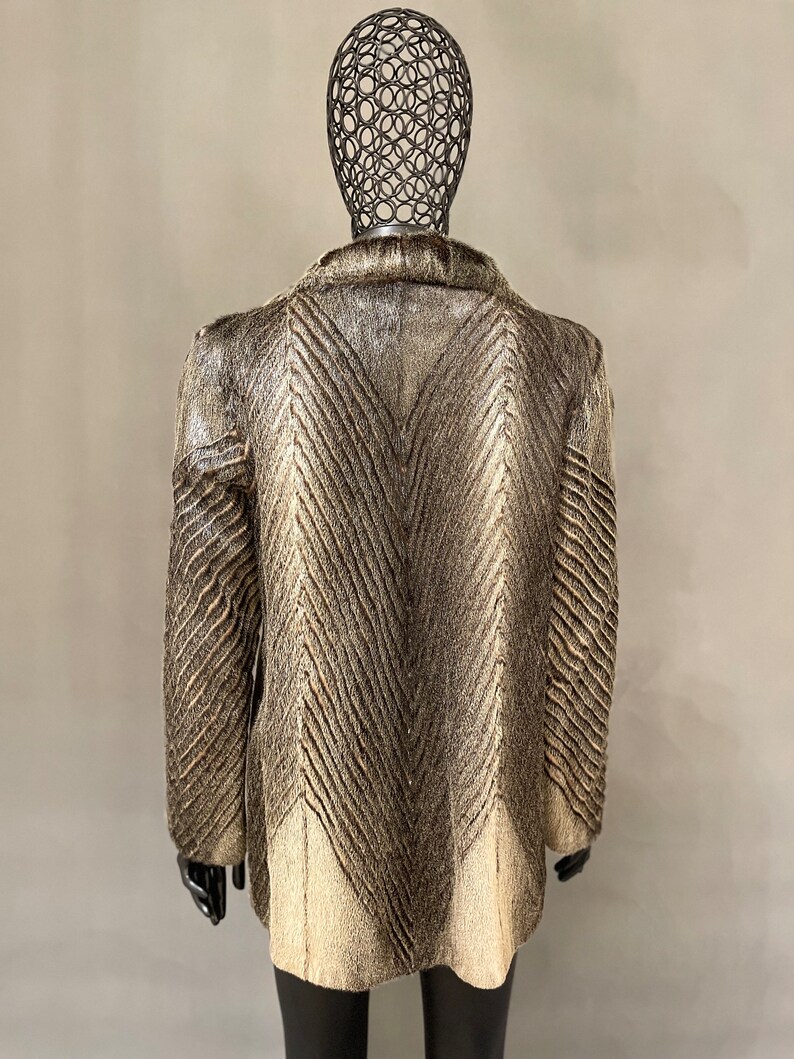 May include: A brown and white fur coat with a chevron pattern. The coat is on a mannequin.