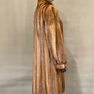 May include: A long brown fur coat with a vertical striped pattern. The coat is on a mannequin.