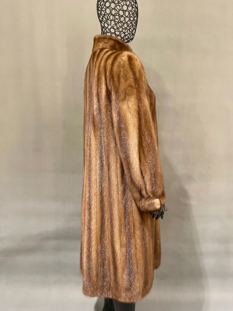 May include: A long brown fur coat with a vertical striped pattern. The coat is on a mannequin.