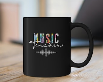 Może przedstawiać: Czarny kubek do kawy z kolorowym nadrukiem "MUSIC teacher" i grafiką fali dźwiękowej.