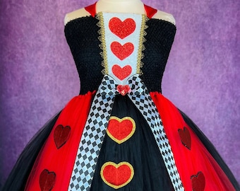 May include: A black and red tulle tutu dress with a black bodice and a white and black checkered ribbon. The bodice has a red heart design with gold glitter accents. The tutu has red hearts with gold glitter accents.