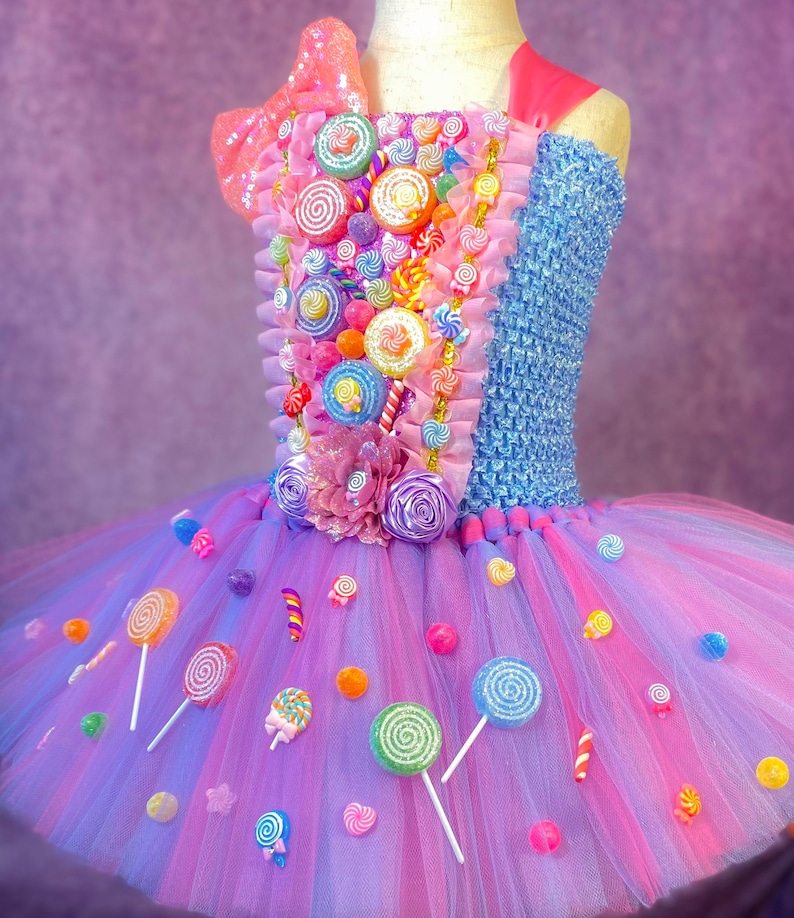 May include: A pink and blue tulle tutu dress decorated with colorful candy, lollipops, and bows. The bodice is blue with a pink and white candy design.