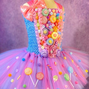 May include: A pink and blue tulle tutu dress with a candy-themed bodice. The bodice is decorated with colorful lollipops, candy canes, and other sweets. The skirt is layered with tulle and has a sparkly pink bow on the top.