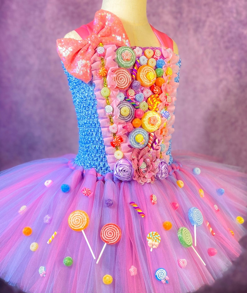 May include: A pink and blue tulle tutu dress with a candy-themed bodice. The bodice is decorated with colorful lollipops, candy canes, and other sweets. The skirt is layered with tulle and has a sparkly pink bow on the top.