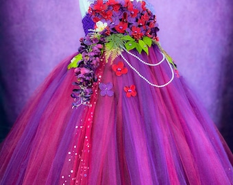 May include: A purple and burgundy tulle dress with a floral bodice. The bodice is adorned with red, purple, and white flowers, as well as green leaves. The dress has a pearl necklace and a tulle skirt.