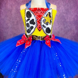 Puede incluir: Un tut&uacute; de tul azul con un corpi&ntilde;o de tem&aacute;tica vaquera amarillo y rojo. El corpi&ntilde;o presenta un pa&ntilde;uelo rojo, una estrella de sheriff y un dise&ntilde;o de estampado de vaca. El tut&uacute; est&aacute; decorado con lentejuelas plateadas.