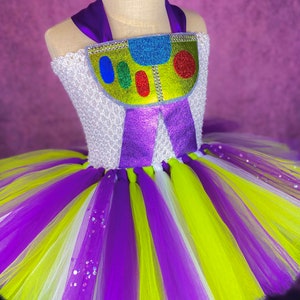 May include: A purple, white, and green tulle tutu with a purple and green bodice featuring a glittery green, yellow, and blue character design.