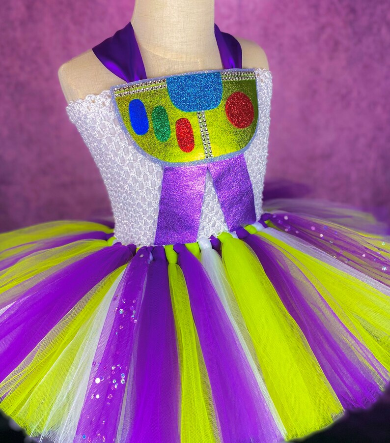 May include: A purple, white, and green tulle tutu with a purple and green bodice featuring a glittery green, yellow, and blue character design.