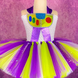 May include: A white tulle tutu with purple, yellow, and white stripes. The tutu has a purple and white bodice with a colorful toy character design.