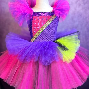 May include: A vibrant tutu dress in shades of pink, purple, and neon green. The bodice features a knitted design with a pink and green geometric pattern, embellished with beads. The skirt is layered with tulle, creating a full, fluffy effect. The dress has matching tulle shoulder accents.