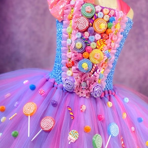 May include: A purple and pink tulle tutu with a candy-themed bodice. The bodice is decorated with colorful lollipops, candy canes, and gumdrops. The tutu is adorned with colorful lollipops and candy.