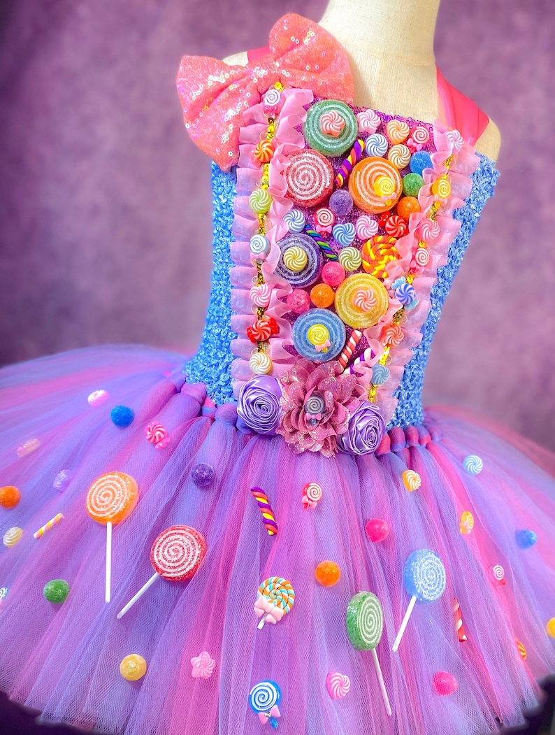 May include: A purple and pink tulle tutu with a candy-themed bodice. The bodice is decorated with colorful lollipops, candy canes, and gumdrops. The tutu is adorned with colorful lollipops and candy.