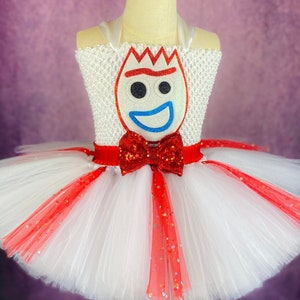 May include: White tulle tutu skirt with red and white stripes and red glitter. The skirt has a red bow with sequins and a felt applique of a character's face with a blue smile.