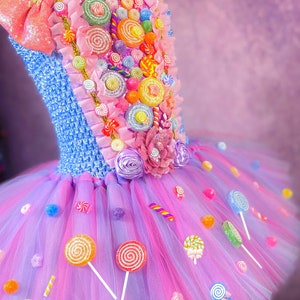 May include: A pink and purple tulle tutu dress decorated with colorful candy, lollipops, and a large bow. The bodice is blue and features a variety of candy decorations.