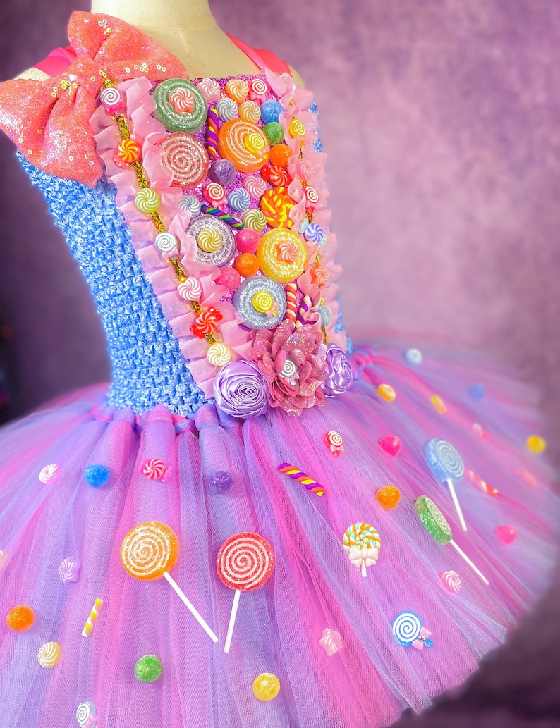 May include: A pink and purple tulle tutu dress decorated with colorful candy, lollipops, and a large bow. The bodice is blue and features a variety of candy decorations.