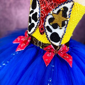 Puede incluir: Un tut&uacute; de tul azul con lazos de bandana rojo y blanco. La parte superior del tut&uacute; es un top de crochet amarillo con un bandana rojo, una impresi&oacute;n de vaca en blanco y negro y una estrella dorada.