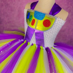 May include: A purple, white, and yellow tulle tutu with a purple and yellow bodice featuring a glittery, colorful toy character design.