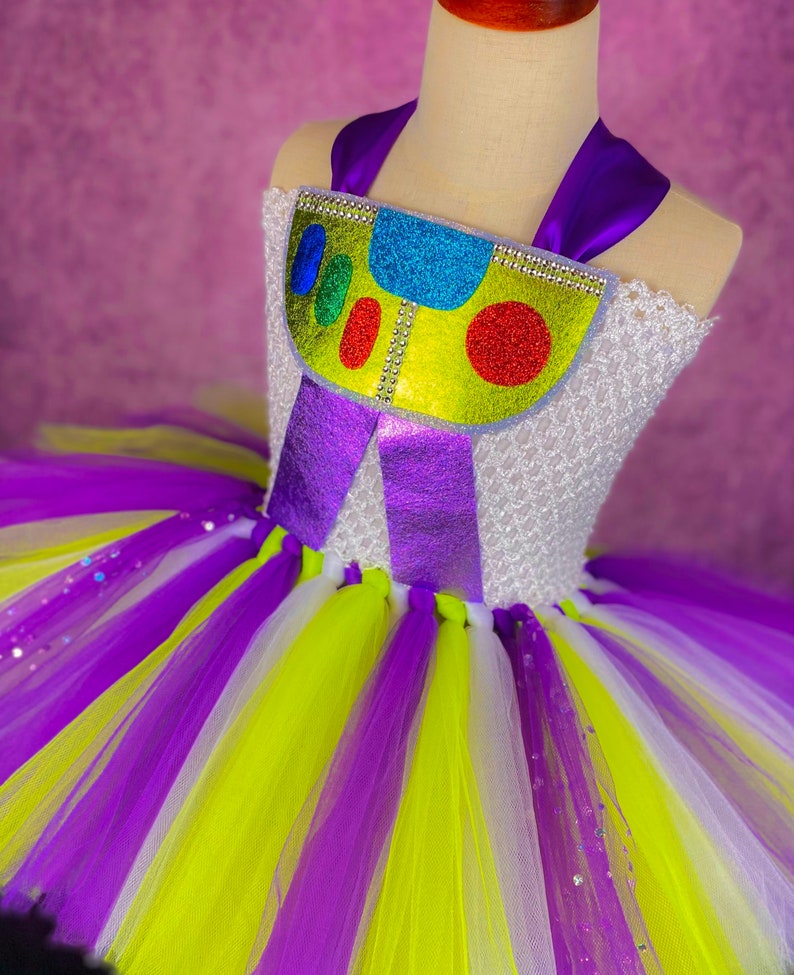 May include: A purple, white, and yellow tulle tutu with a purple and yellow bodice featuring a glittery, colorful toy character design.