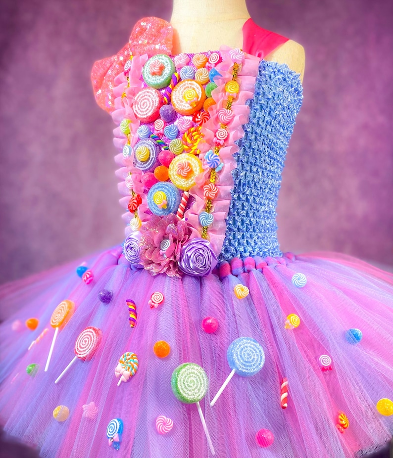 May include: A pink and purple tulle tutu dress decorated with colorful candy, lollipops, and sprinkles. The bodice is blue and features a variety of candy decorations.