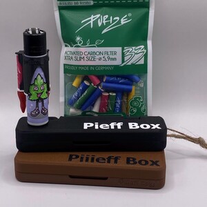 Puede incluir: Un encendedor negro y verde con un personaje de dibujos animados, una caja negra con el texto "Pieff Box" en ella, una caja marrón con el texto "Piiieff Box" en ella y una bolsa de filtros de carbón activado verde, azul y rojo con el texto "PURIZE" en ella.