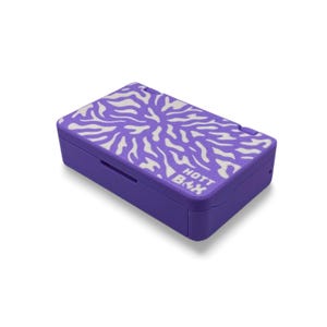 Puede incluir: Una caja de almacenamiento rectangular de color morado con una tapa abatible que presenta un patrón radial abstracto en blanco. El texto HOTT BOX está impreso en blanco en la esquina superior derecha de la tapa. La caja tiene un acabado mate.