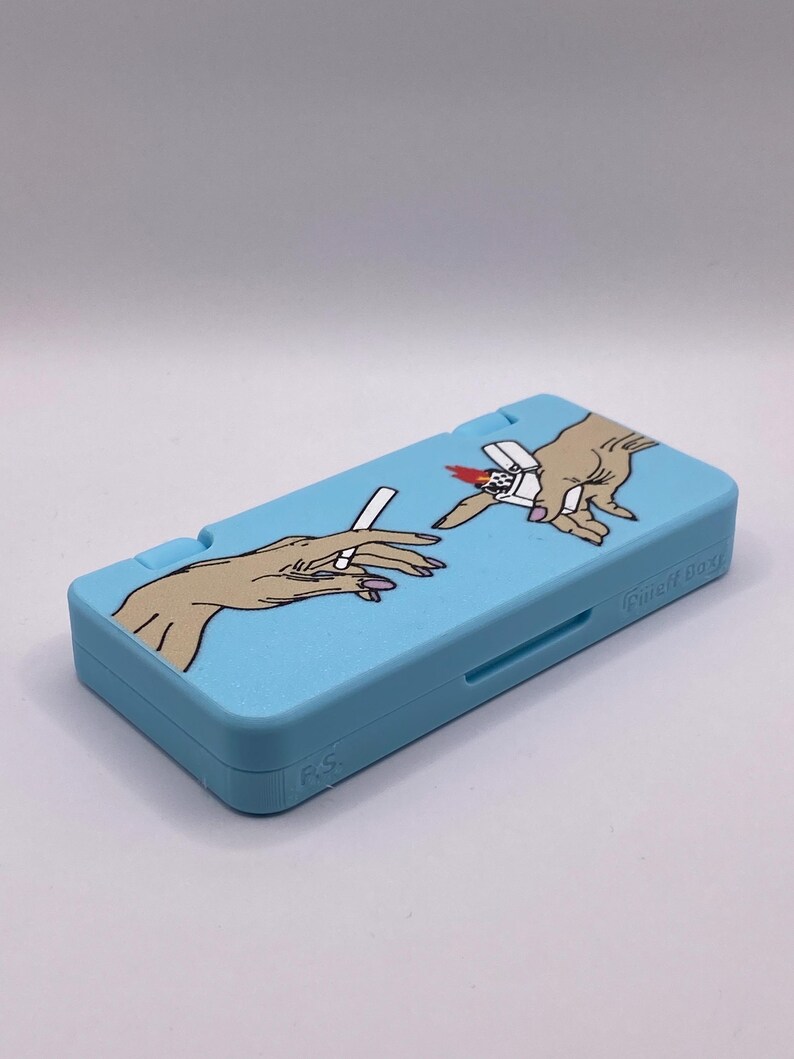 May include: A light blue Nintendo DS case with a graphic of two hands holding a cigarette and a lighter. The case has the text "Guilty Gear" printed on the side.