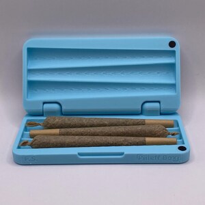 May include: A light blue, rectangular, plastic case with a black dot on the top right corner. The case is open and has four brown, rolled cigarettes inside. The case has the text "Pliff Box" on the bottom right corner and "FCS" on the bottom left corner.