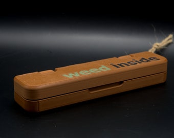 May include: A brown wooden box with a hinged lid. The box has the words "weed inside" printed on the top in green letters.