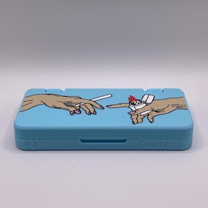 May include: A light blue Nintendo Switch game case with a graphic of two hands, one holding a cigarette and the other holding a lighter. The case has the text "Pilljeff Boxy" on the bottom right corner.