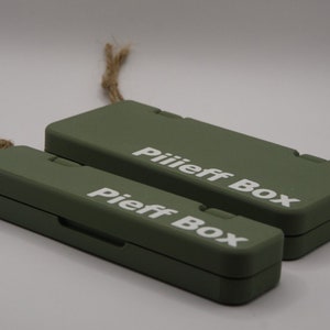 Pu&ograve; includere: Due scatole rettangolari verdi con il testo "Pieff Box" e "Piiiieff Box" stampato in bianco. Le scatole sono realizzate in un materiale robusto e hanno un design semplice e moderno.