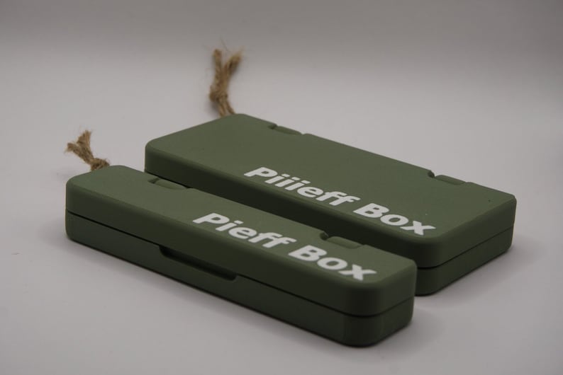 Pu&ograve; includere: Due scatole rettangolari verdi con il testo "Pieff Box" e "Piiiieff Box" stampato in bianco. Le scatole sono realizzate in un materiale robusto e hanno un design semplice e moderno.