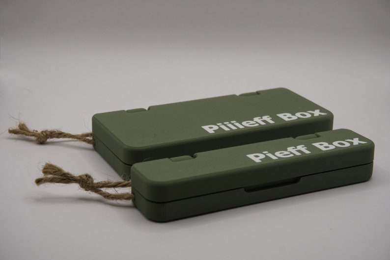 Pu&ograve; includere: Due scatole rettangolari verdi con un manico in corda. La scatola superiore ha il testo "Piliieff Box" stampato su di essa. La scatola inferiore ha il testo "Pieff Box" stampato su di essa.