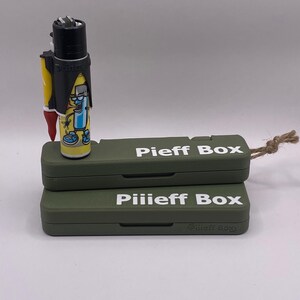 Pu&ograve; includere: Due scatole verdi con il testo "Pieff Box" e "Pilieff Box" stampato in bianco sul davanti. Un accendino nero con un personaggio dei cartoni animati sopra &egrave; seduto sopra le scatole.